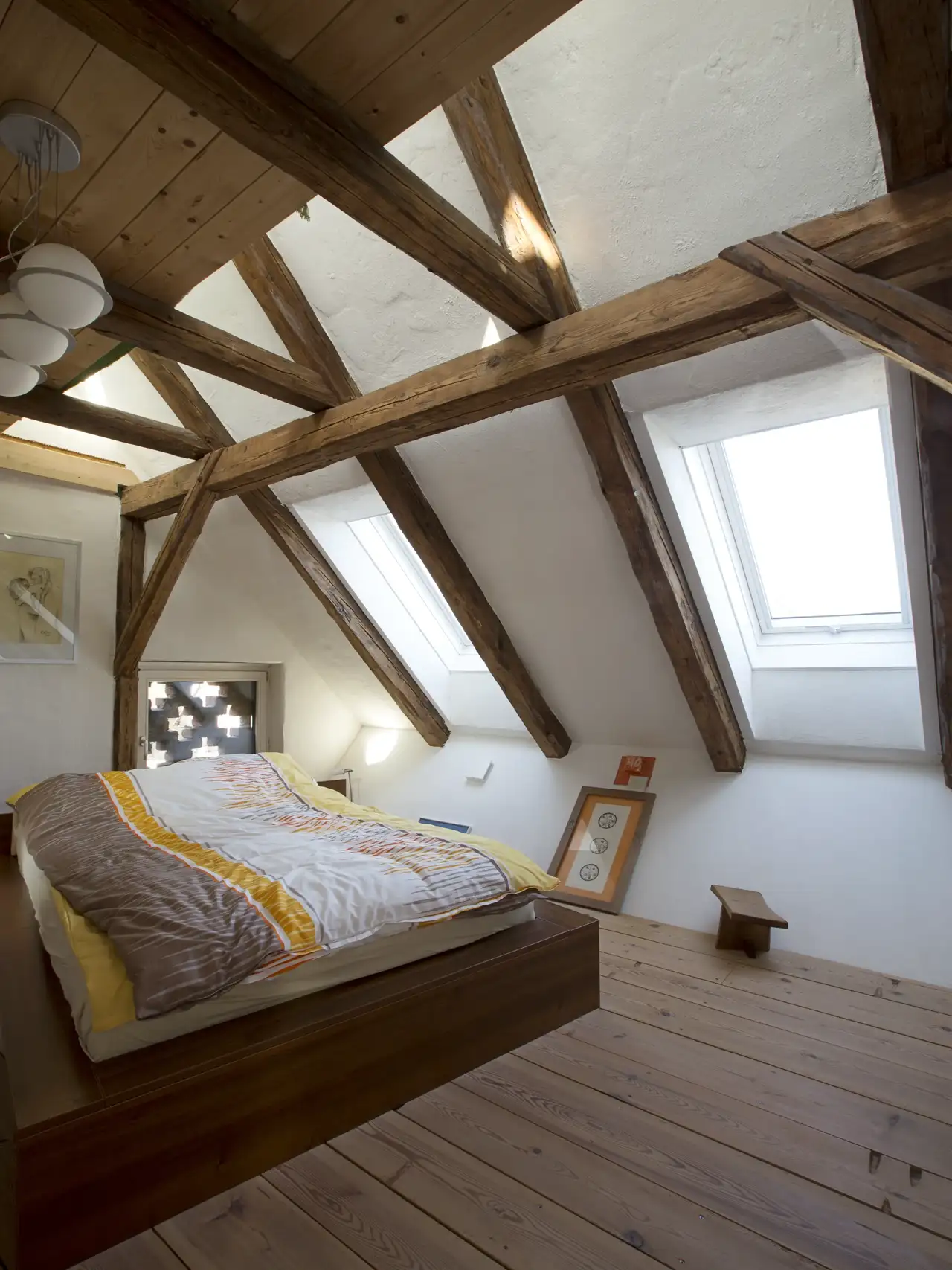 Camera mansardata in stile rustico con travi in legno, pavimento naturale e finestre per tetti che illuminano lo spazio.