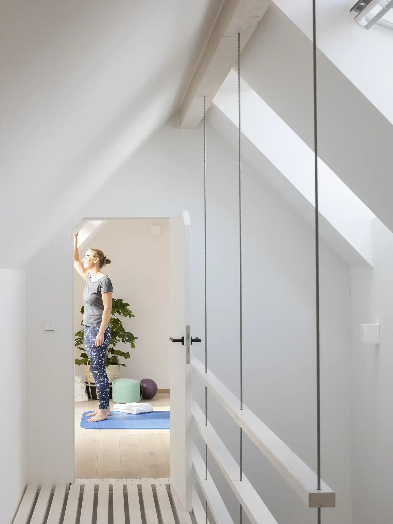 Frau steht auf Yogamatte im offenen Spitzboden mit Galerie und schaut aus dem Fenster| VELUX Magazin