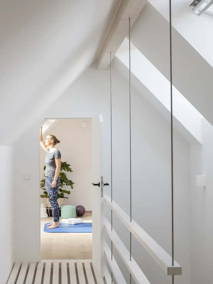 Frau steht auf Yogamatte im offenen Spitzboden mit Galerie und schaut aus dem Fenster| VELUX Magazin