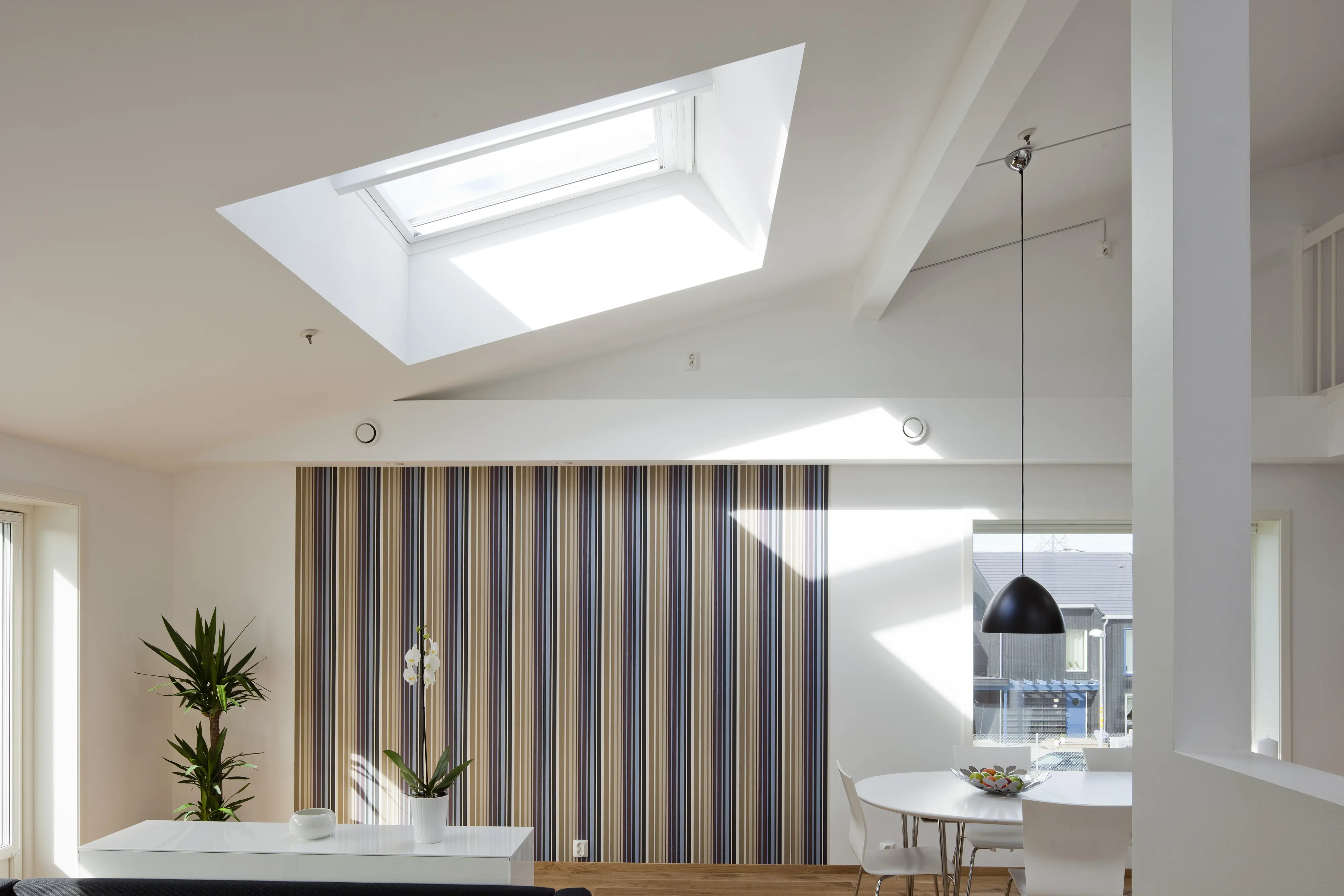 Zonă de luat masa cu fereastră de mansardă VELUX, tapet cu dungi și decor modern.