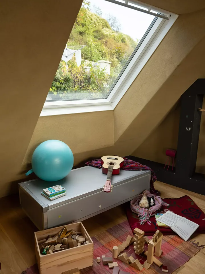 Sitzbank unter Dachfenster vor buntem Teppich, umgeben von Holzbauklötzen, Kindergitarre, Spielball und Büchern | VELUX Magazin