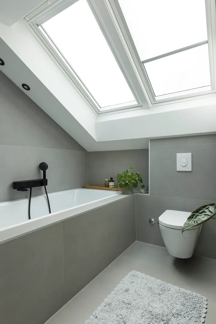  Svijetla kupaonica u potkrovlju sa sivim pločicama i krovnim prozorima iznad kade i WC-a | VELUX