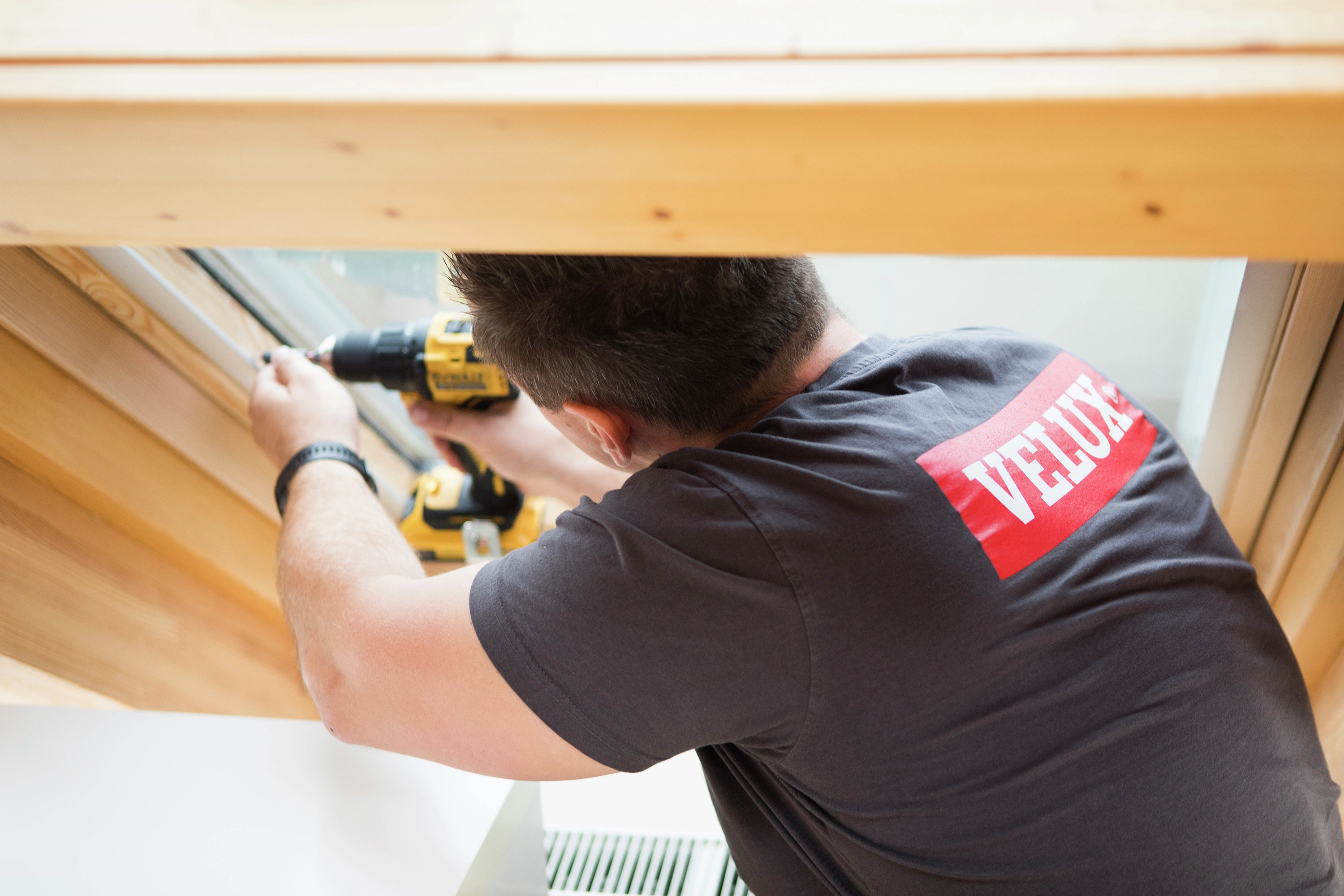 Installer working on VELUX roof window with drill, wearing VELUX shirt.