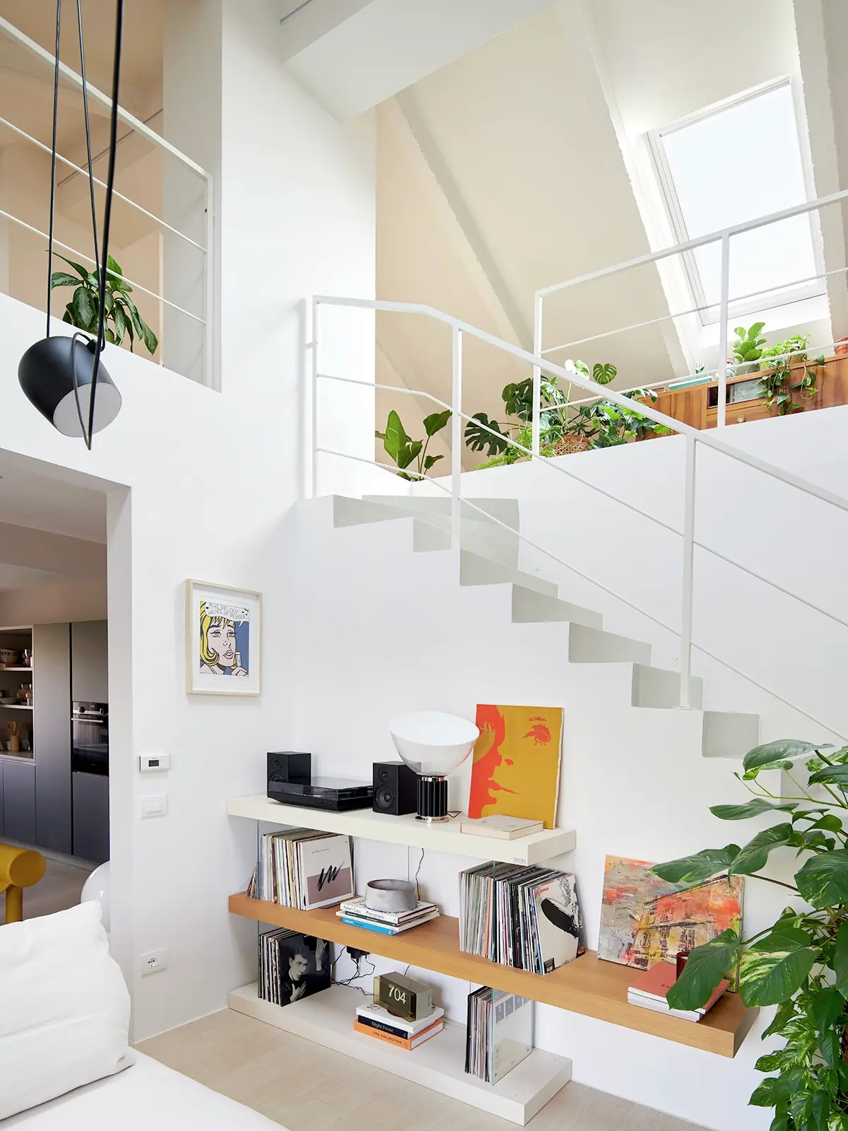 Zona scala luminosa con finestra per tetti VELUX, scaffali in legno, piante e vista nella cucina.