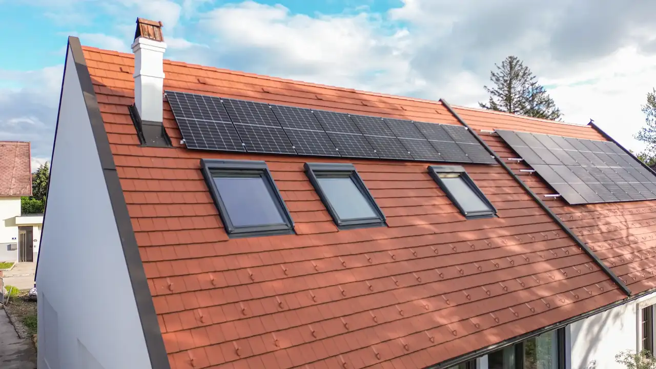 Ein Haus mit einem rot gedeckten Dach, mehreren VELUX Dachfenstern und Solarpanelen, vor einem teils bewölkten Himmel. | VELUX Magazin