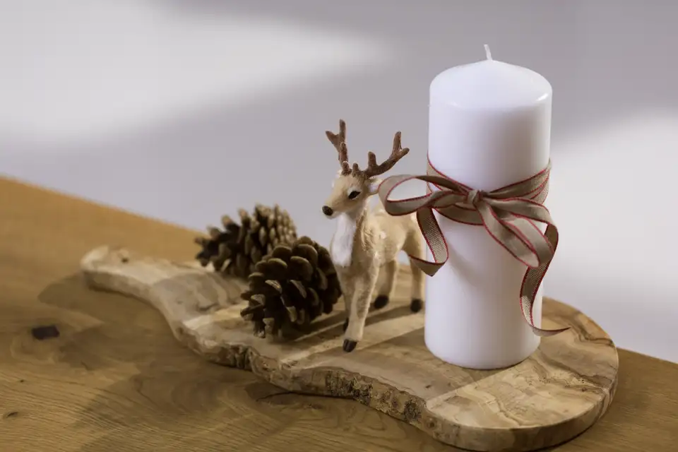 Candela bianca con nastro e piccola renna su base in legno, decorazione naturale per la tavola delle feste.