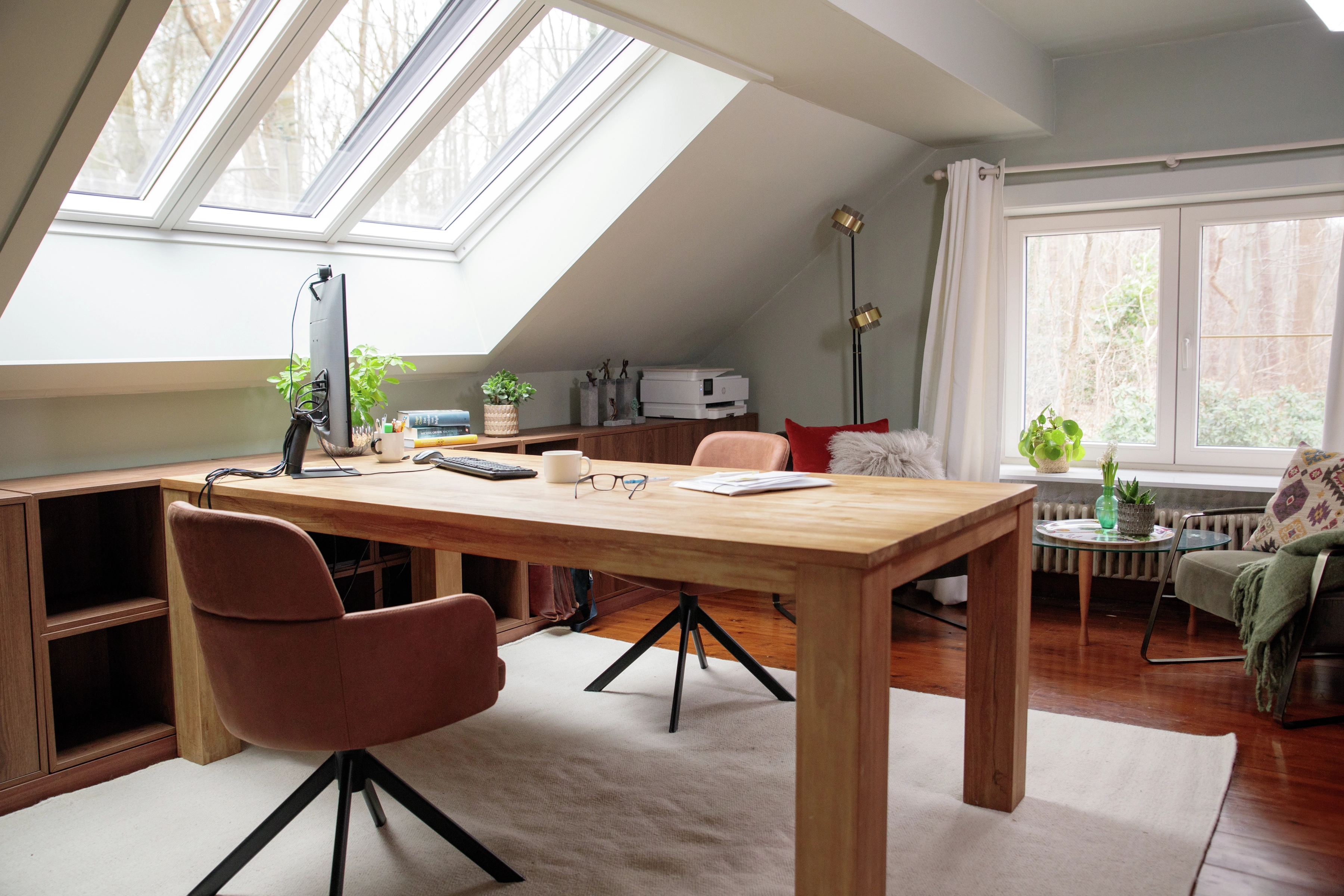 Attic home office with sloped ceiling and VELUX roof window, wooden desk and chairs.