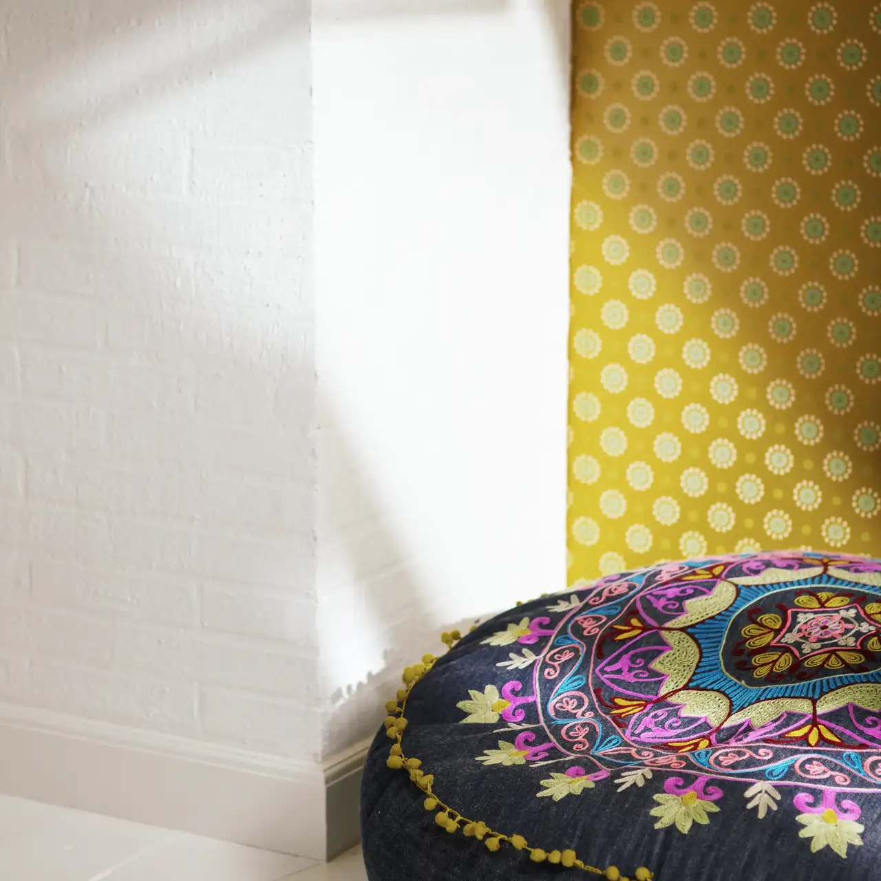 Bunt besticktes schwarzes Boho-Kissen vor Wand mit gelbgemusterter Tapete | VELUX Magazin
