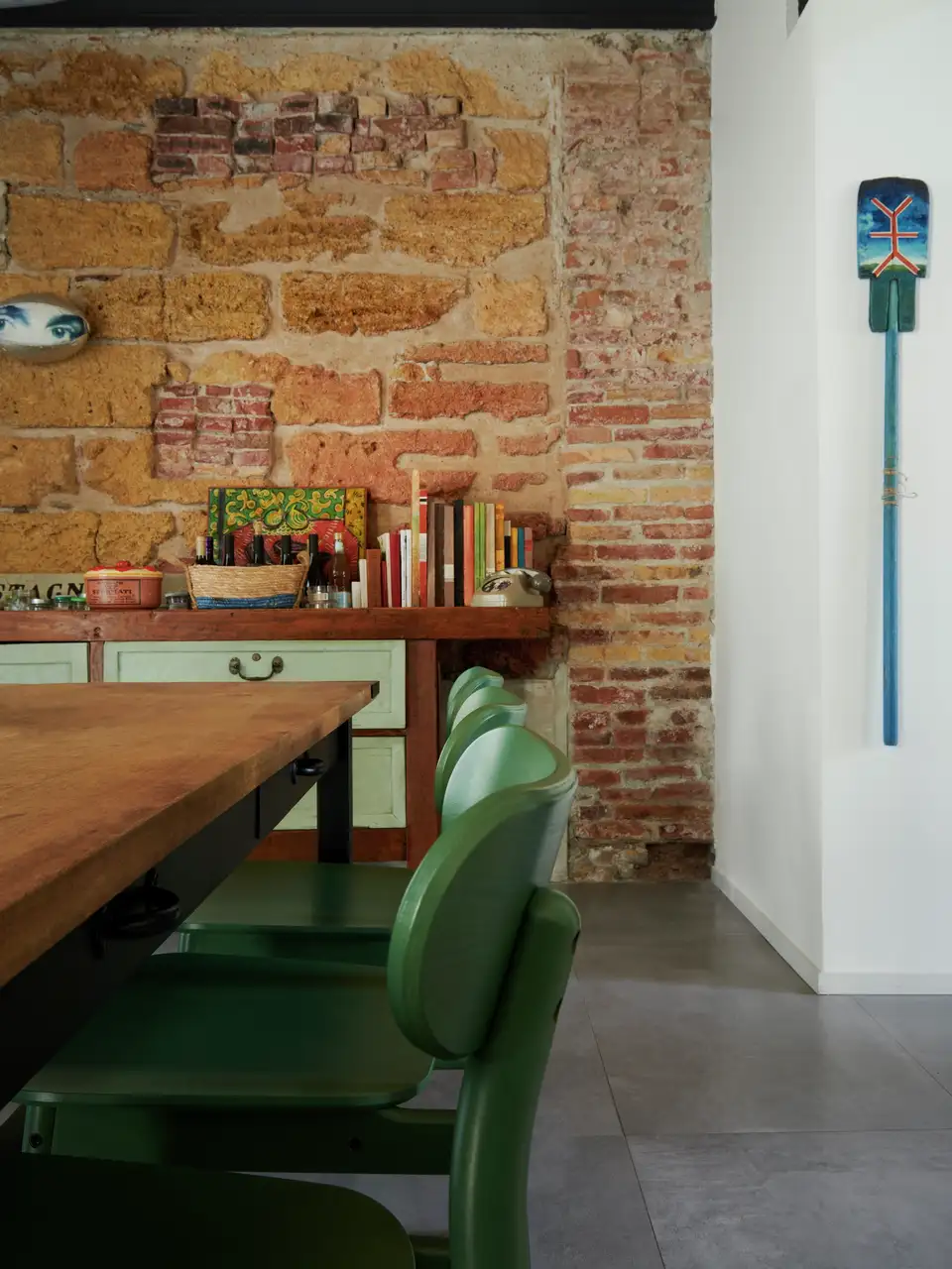 Dining room with exposed brick walls, wooden table, and green chairs. 