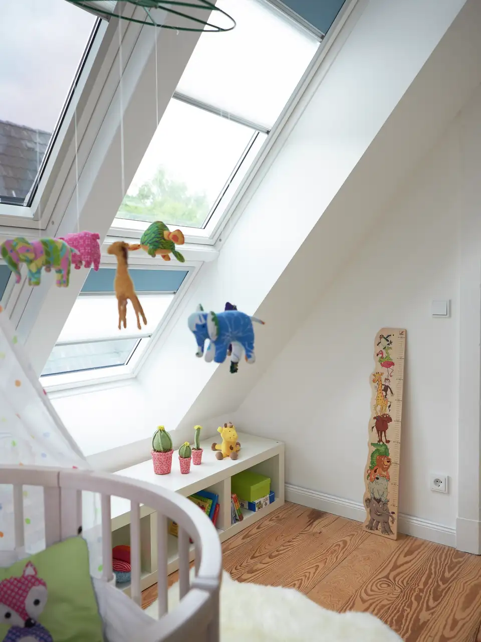 Chambre de bébé éclairée par trois fenêtres de toit VELUX, aménagée avec des matériaux et couleurs naturels.