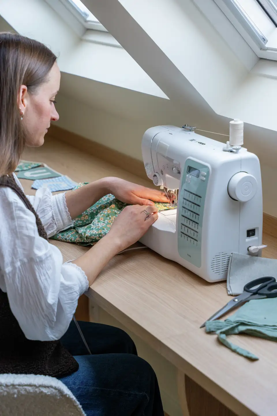 Femme utilisant une machine à coudre sous deux fenêtres de toit VELUX. 