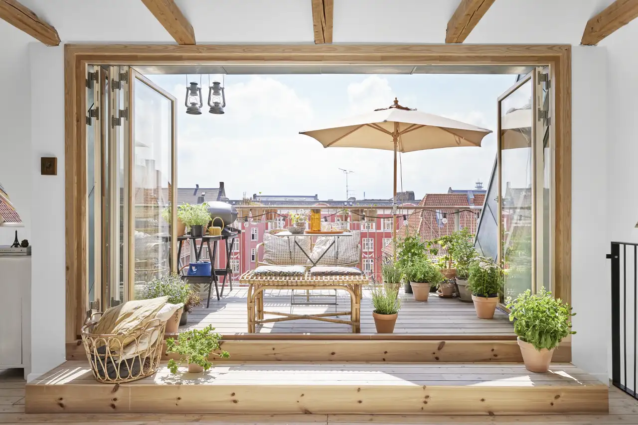 Une terrasse aménagée avec transats, parasol, barbecue et plantes en pot.