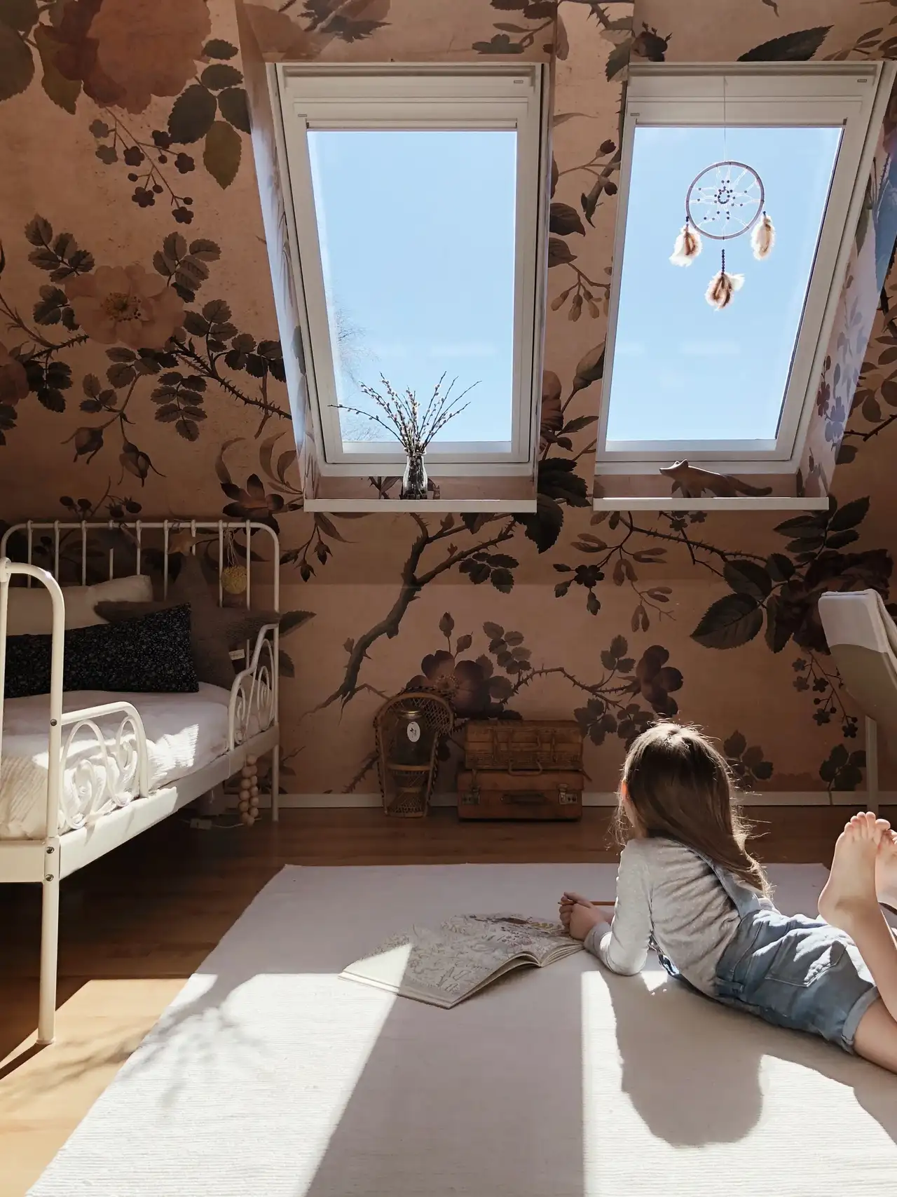 Attic room with floral wallpaper, VELUX windows, and child reading.