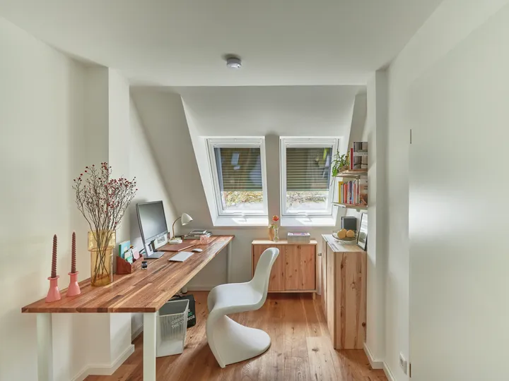 Dachboden-Heimbüro mit natürlichem Licht von VELUX Dachflächenfenstern, hölzernem Schreibtisch und Bücherregal.
