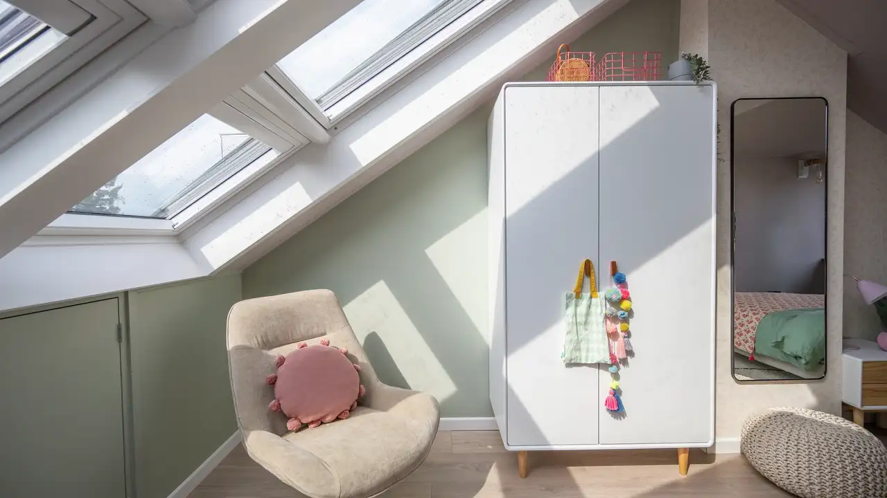 Camera da letto in mansarda con grandi finestre per tetti VELUX, arredi e colori chiari e un grande specchio.