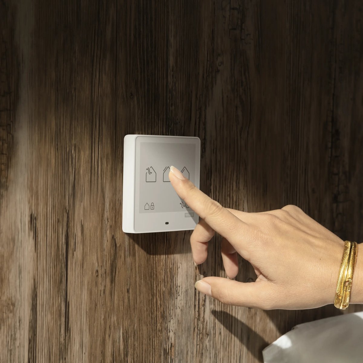 Hand interacting with smart home control panel on wooden wall.
