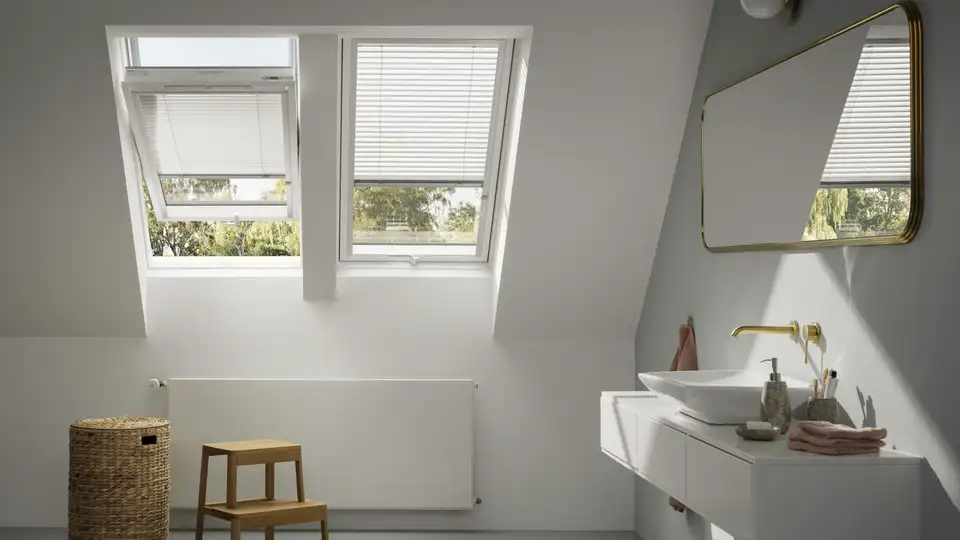 salle de bains mansardée avec deux fenêtres de toit VELUX équipées de stores vénitiens blancs partiellement relevés