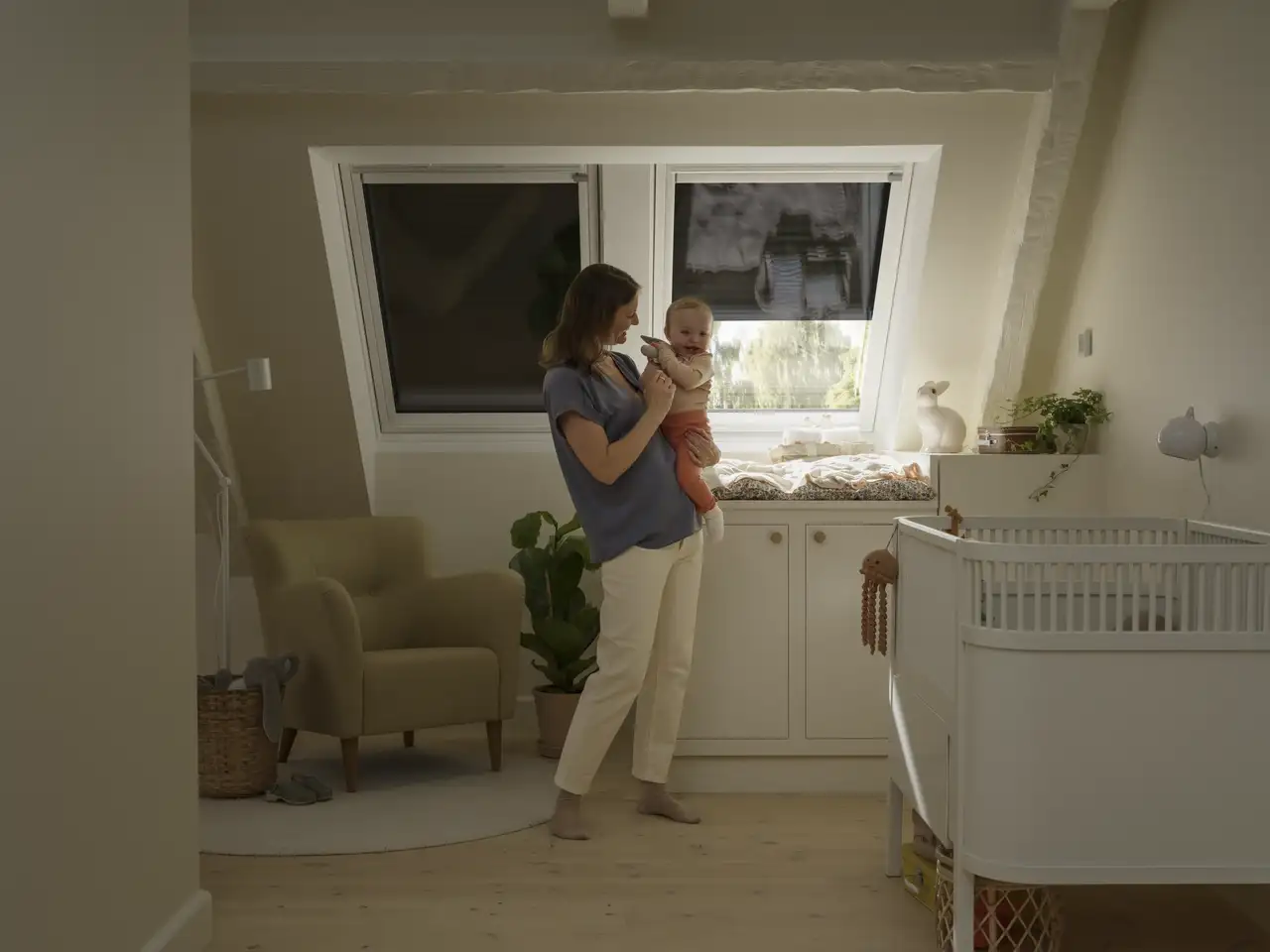 Une femme et un nourrisson dans une chambre équipée de fenêtres de toit avec volets roulants, qui permettent de contrôler la chaleur entrante et d’assombrir la pièce. 