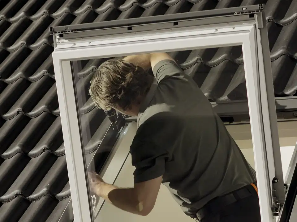 Installatore monta una finestra per tetti VELUX su un tetto a falde con tegole nere.