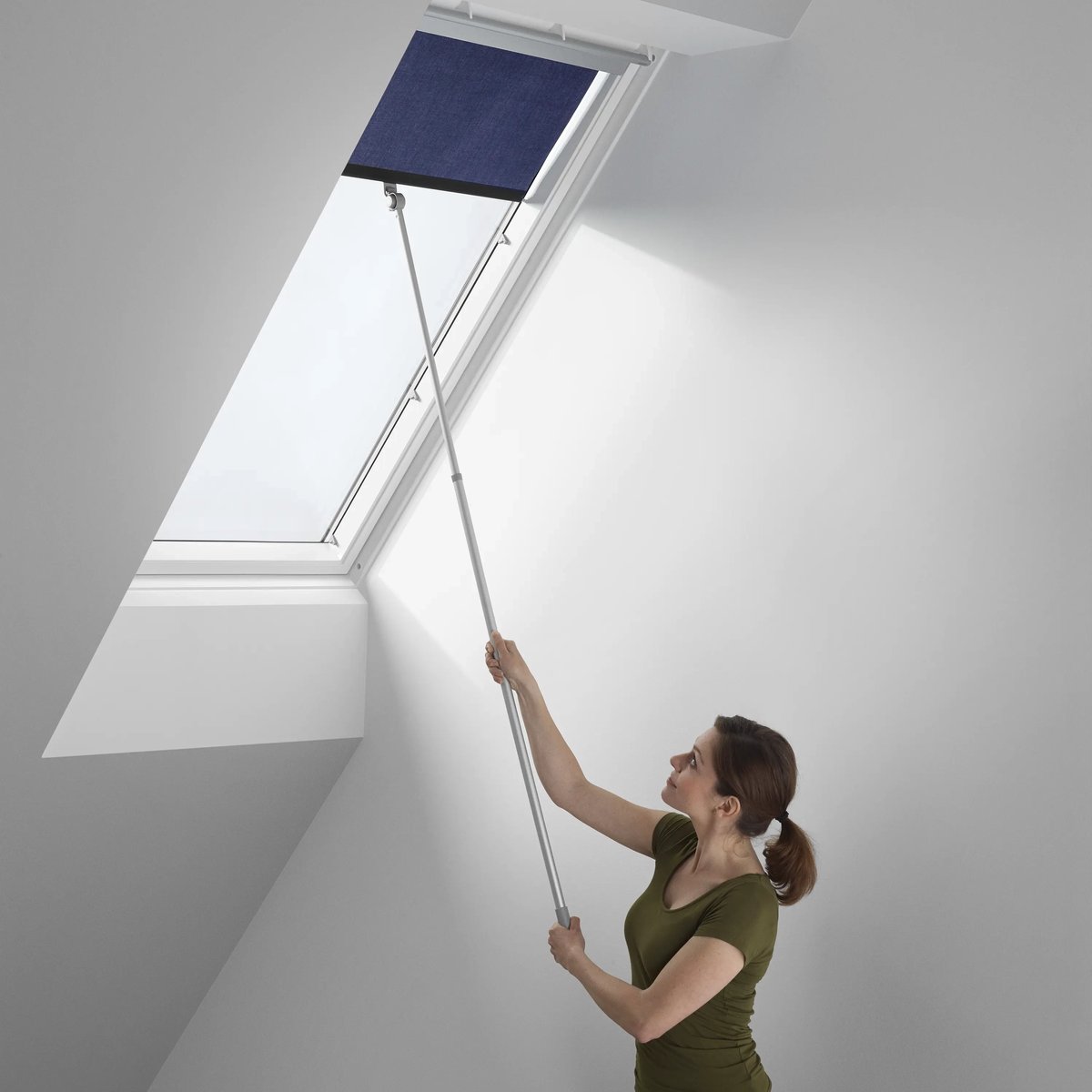 Attic room with sloped ceiling and VELUX roof window, person adjusting blind.