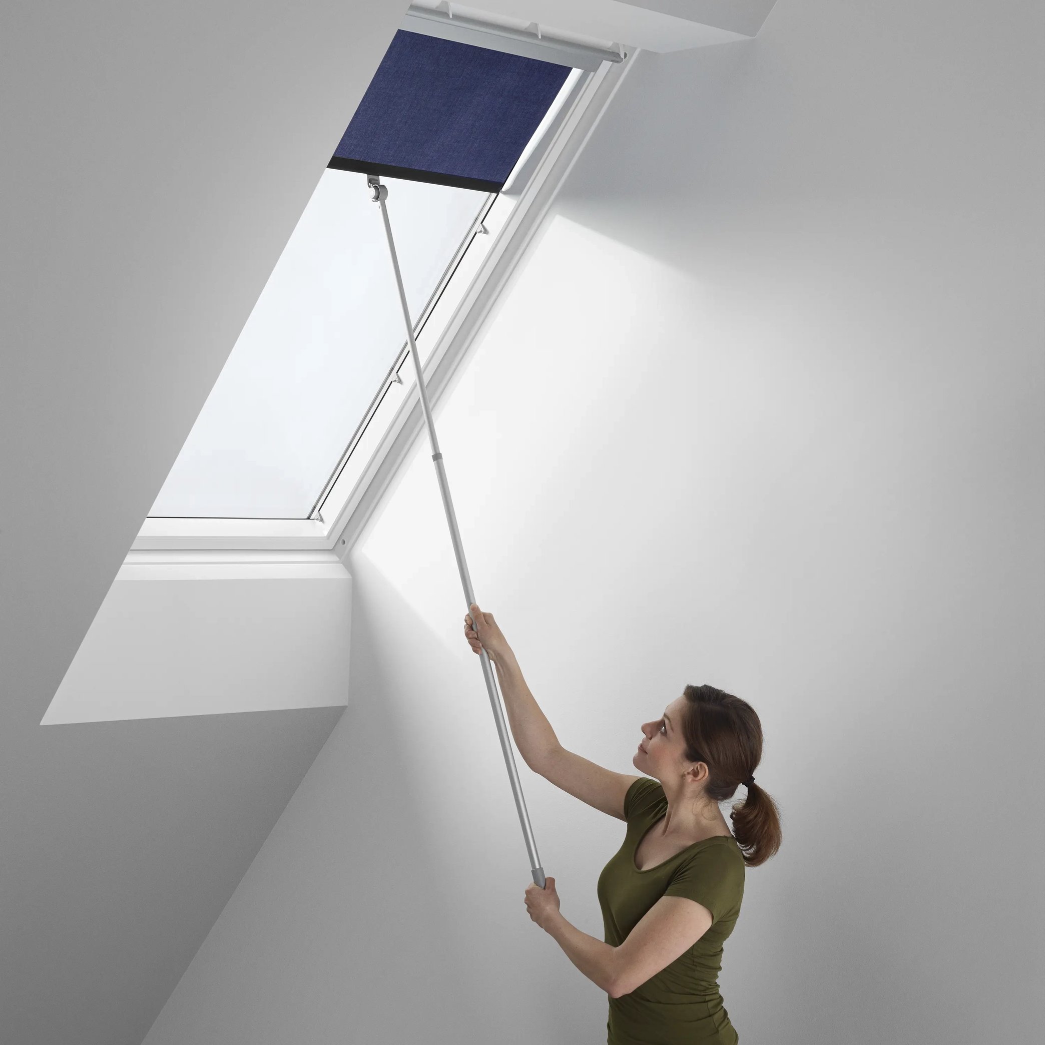 Attic room with sloped ceiling and VELUX roof window, person adjusting blind.