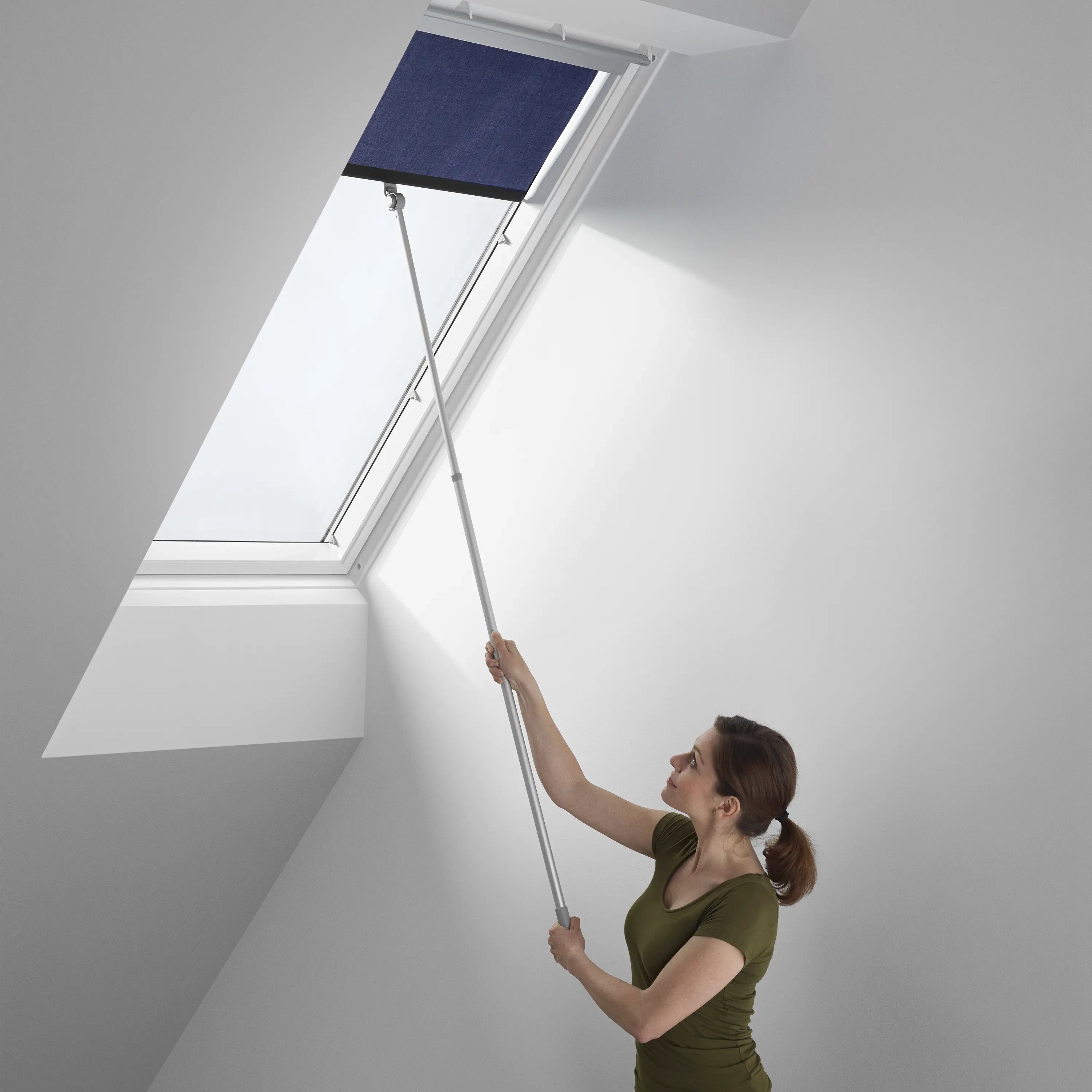 Attic room with sloped ceiling and VELUX roof window, person adjusting blind.