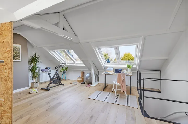 Работно място на таванско помещение със скосен таван и покривни прозорци VELUX, бюро и велоергометър.