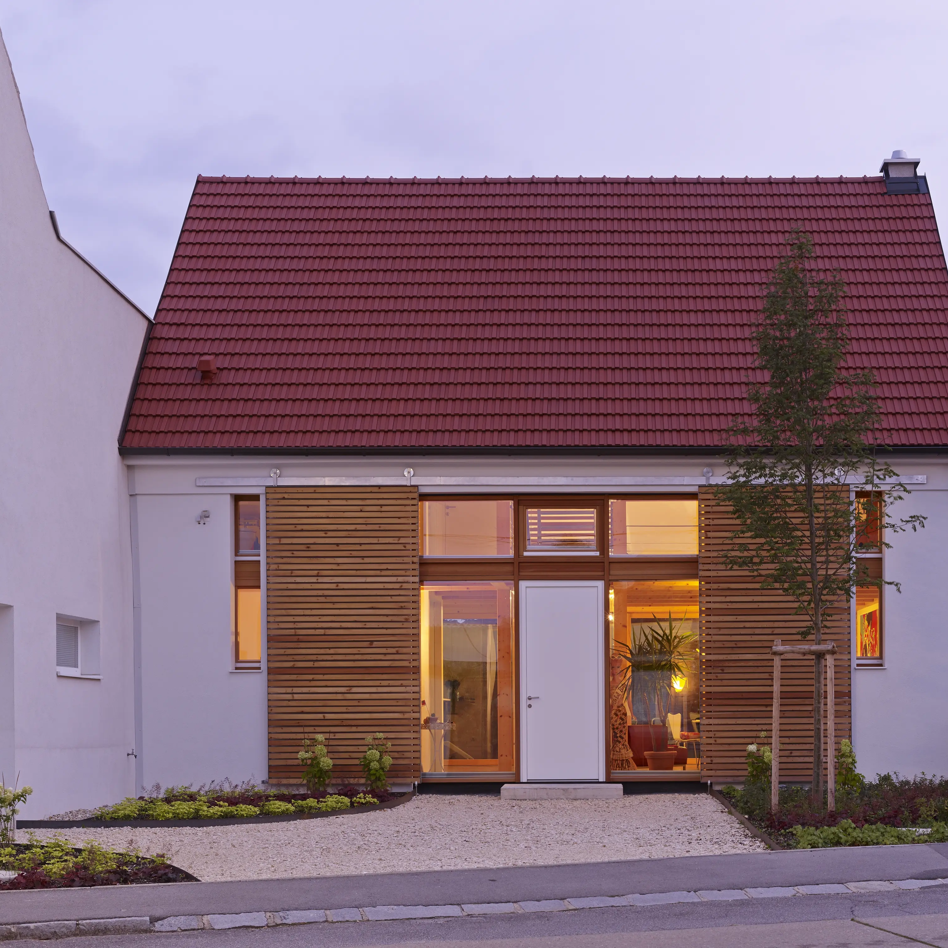 Single-family house with red tile roof and large windows, warm interior lighting.