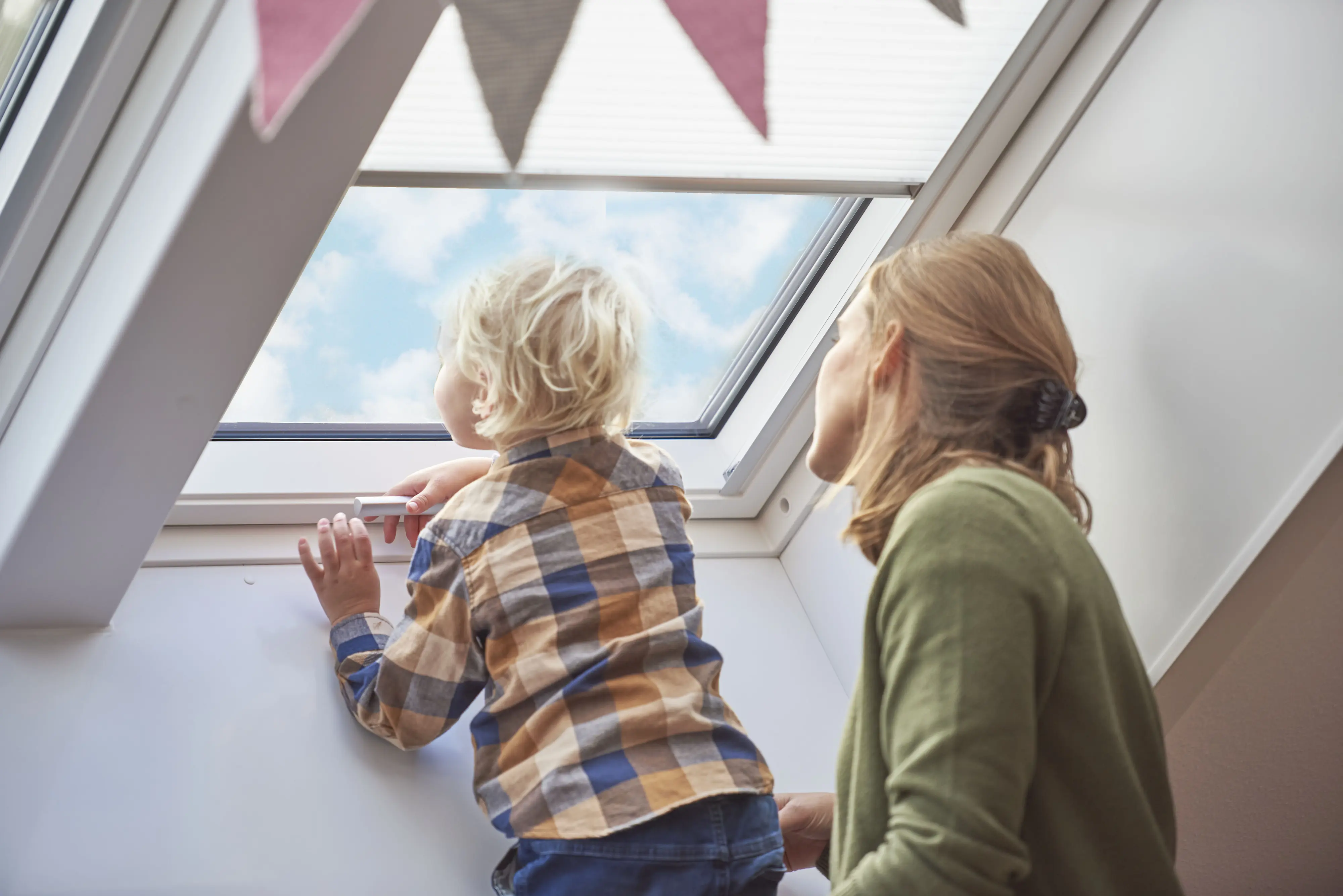 Matka a dieťa v podkrovnej izbe s otvoreným strešným oknom VELUX.