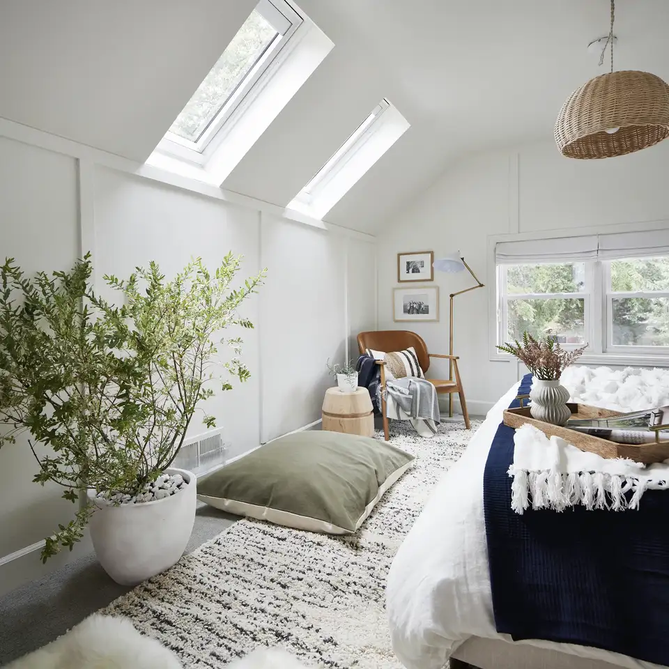 Attic bedroom with sloped ceiling and VELUX roof windows, natural light entering.