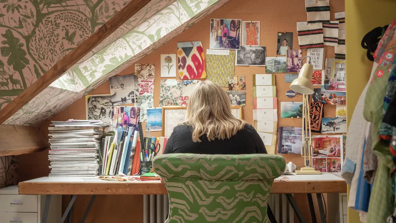 Attic workspace with sloped ceiling, desk, and corkboard filled with creative materials.