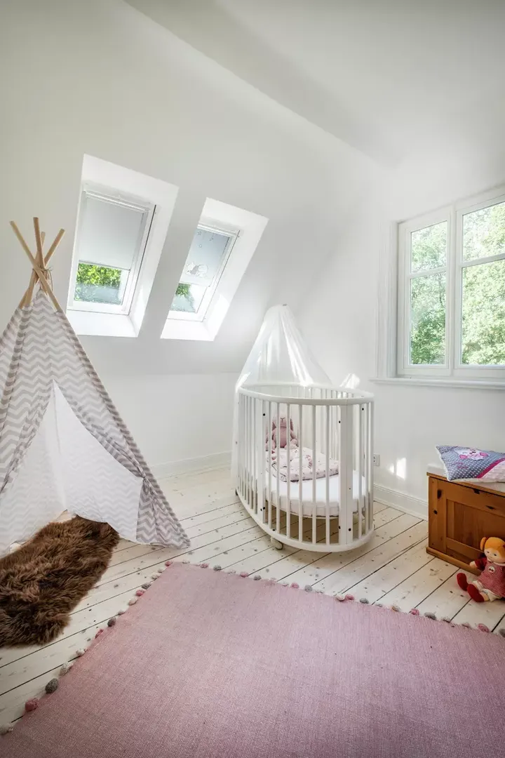 Helles Kinderzimmer mit VELUX Dachflächenfenstern, Spielzelt, runder Krippe und rosa Teppich.