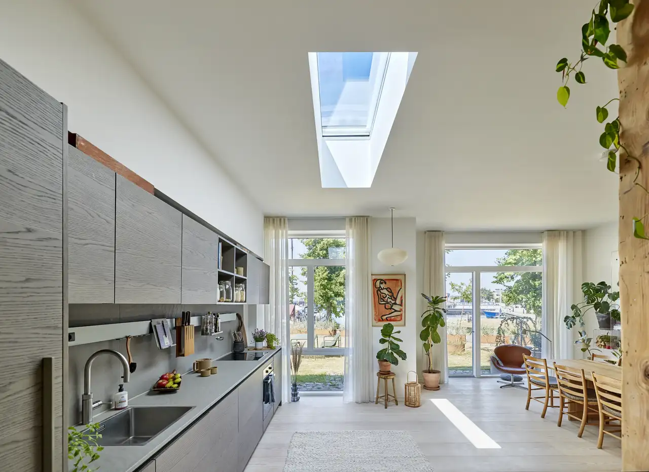 Cucina moderna con finestra per tetti piani VELUX e grandi finestre verticali con vista su giardino.