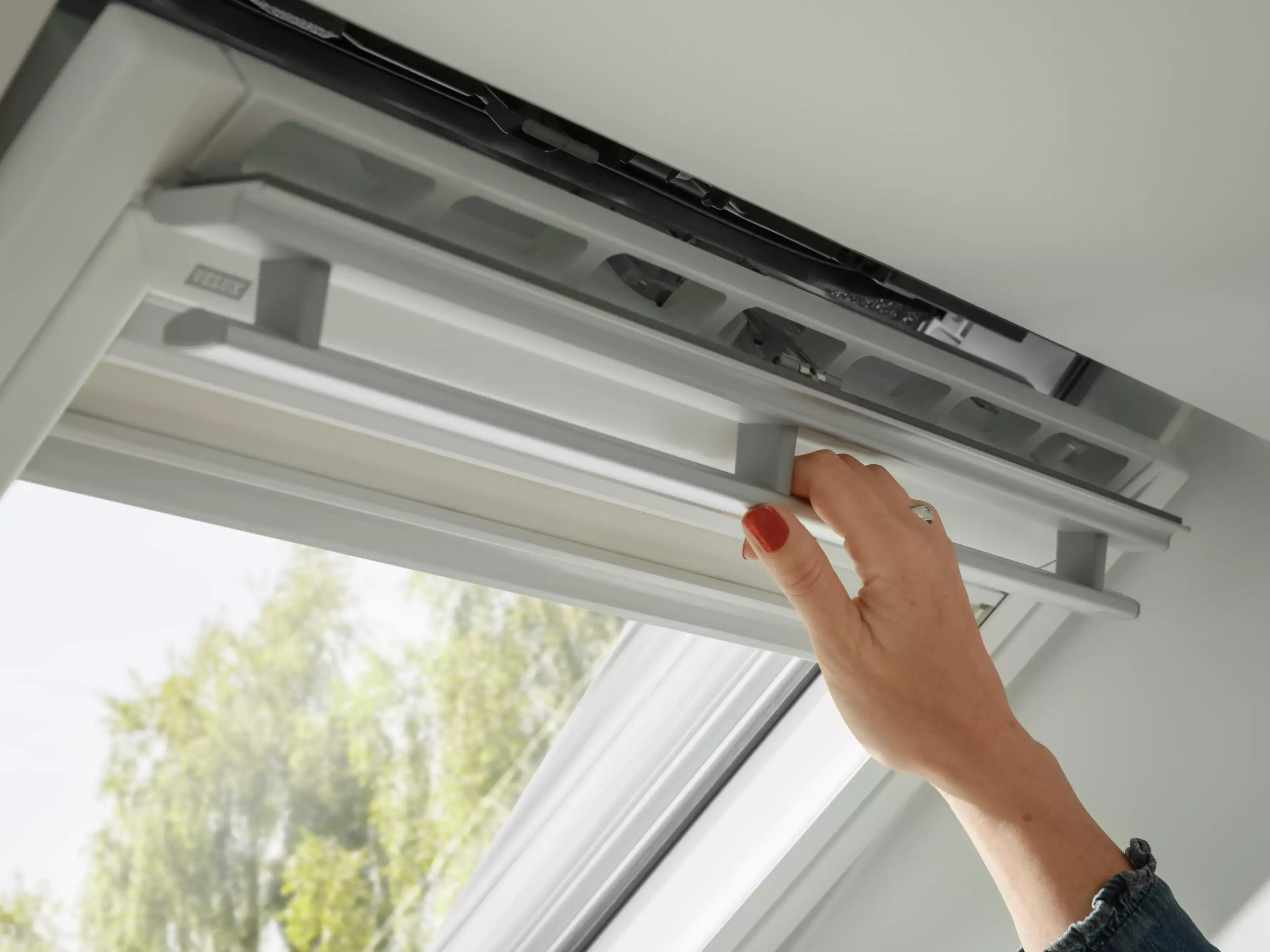 Main ajustant une fenêtre de toit VELUX moderne, laissant entrer la lumière naturelle.