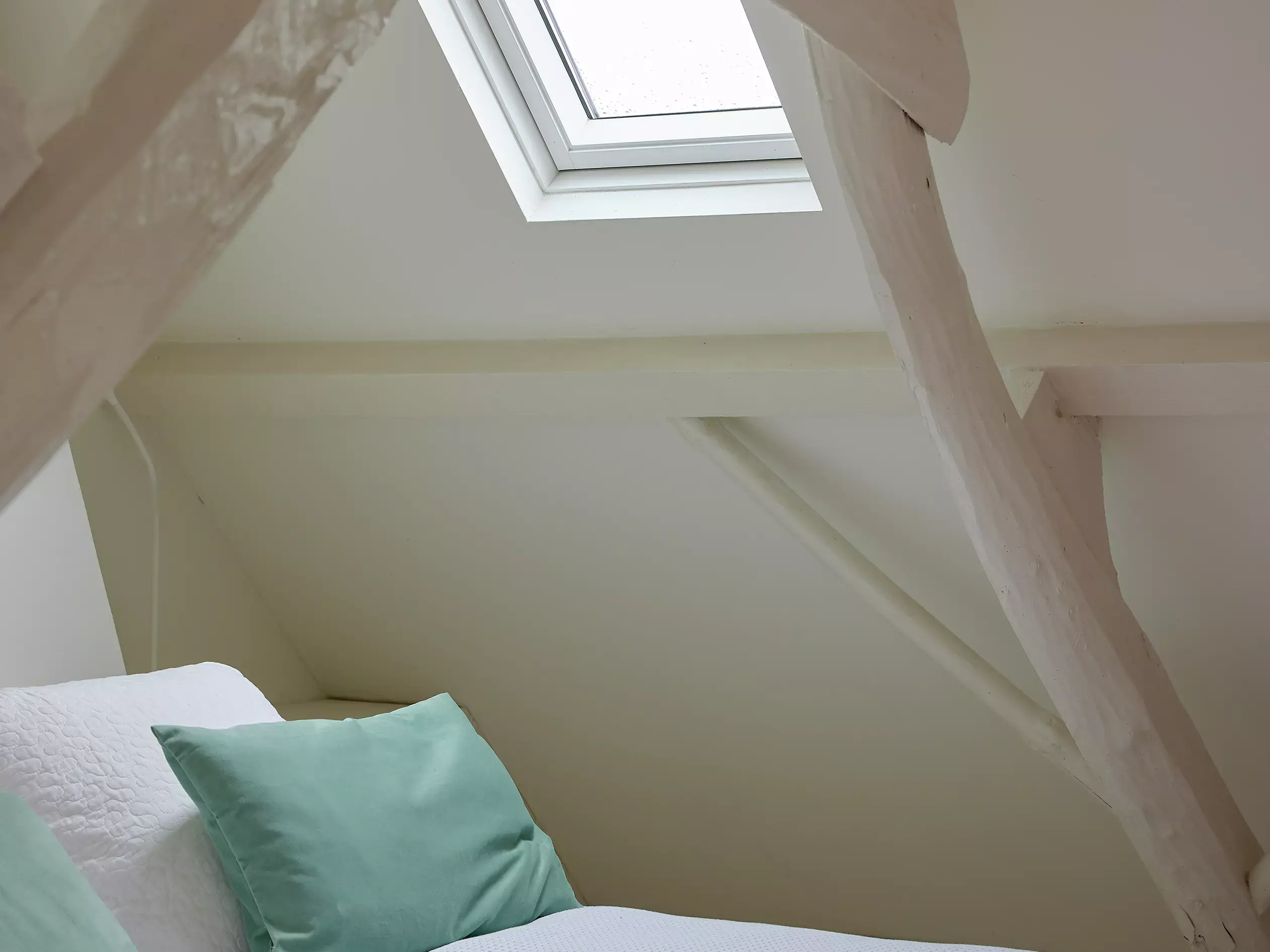 Chambre de comble avec literie blanche, coussin vert et une fenêtre de toit VELUX.