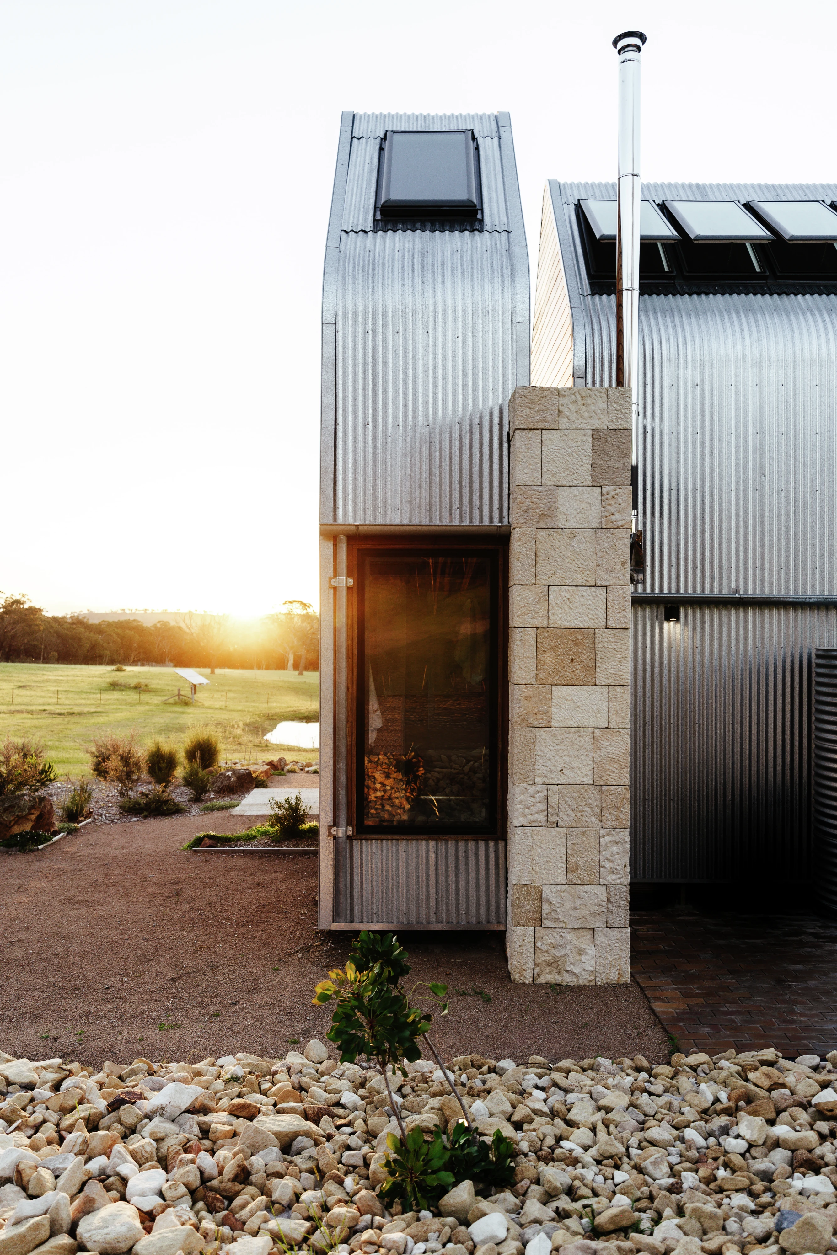 Modern corrugated metal house with VELUX roof windows at sunset in a rural landscape.