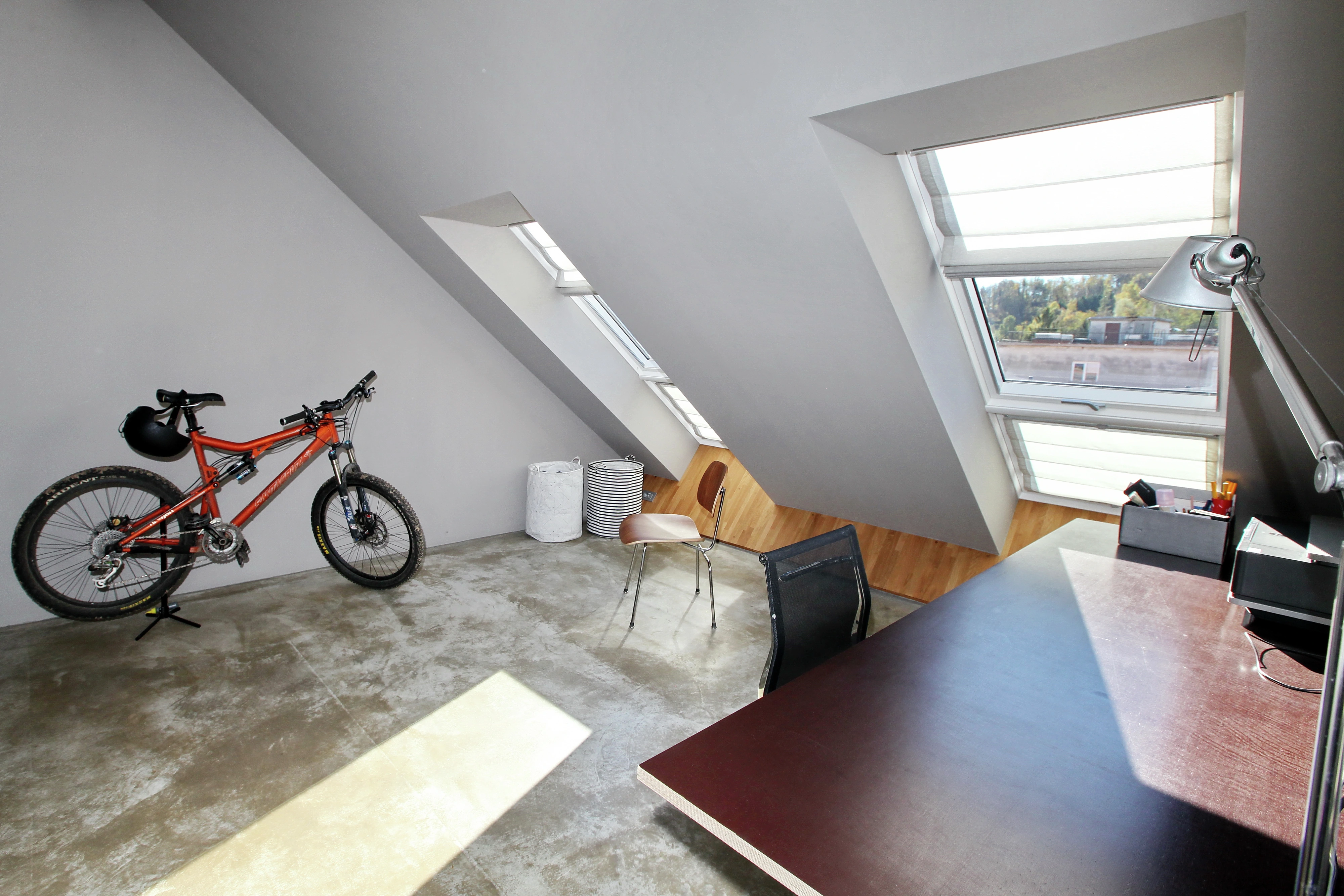 Attic room with sloped ceiling, VELUX window, desk, chair, and bicycle.