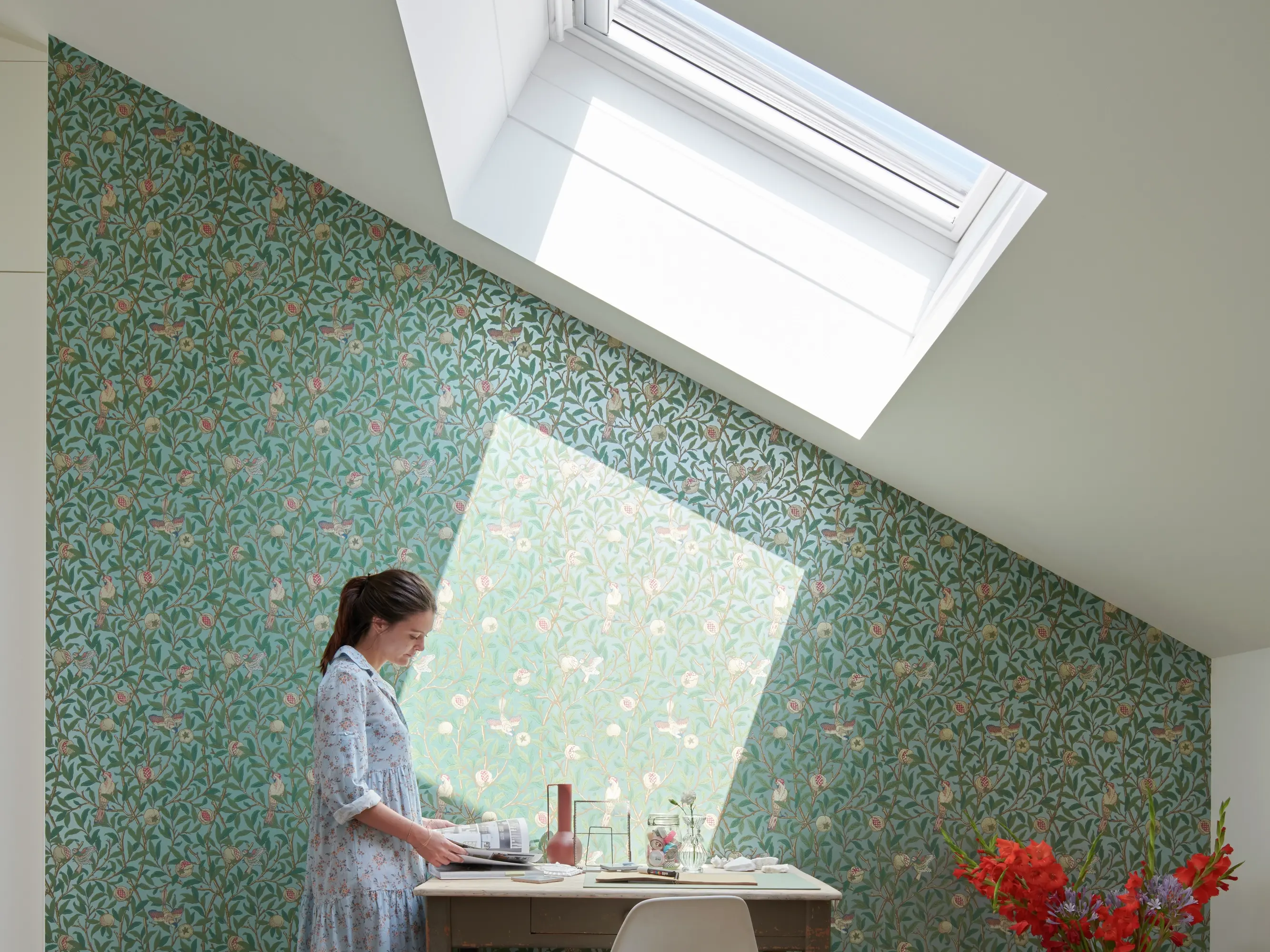 Bureau à domicile avec fenêtre de toit VELUX et papier peint floral, créant un espace de travail lumineux.