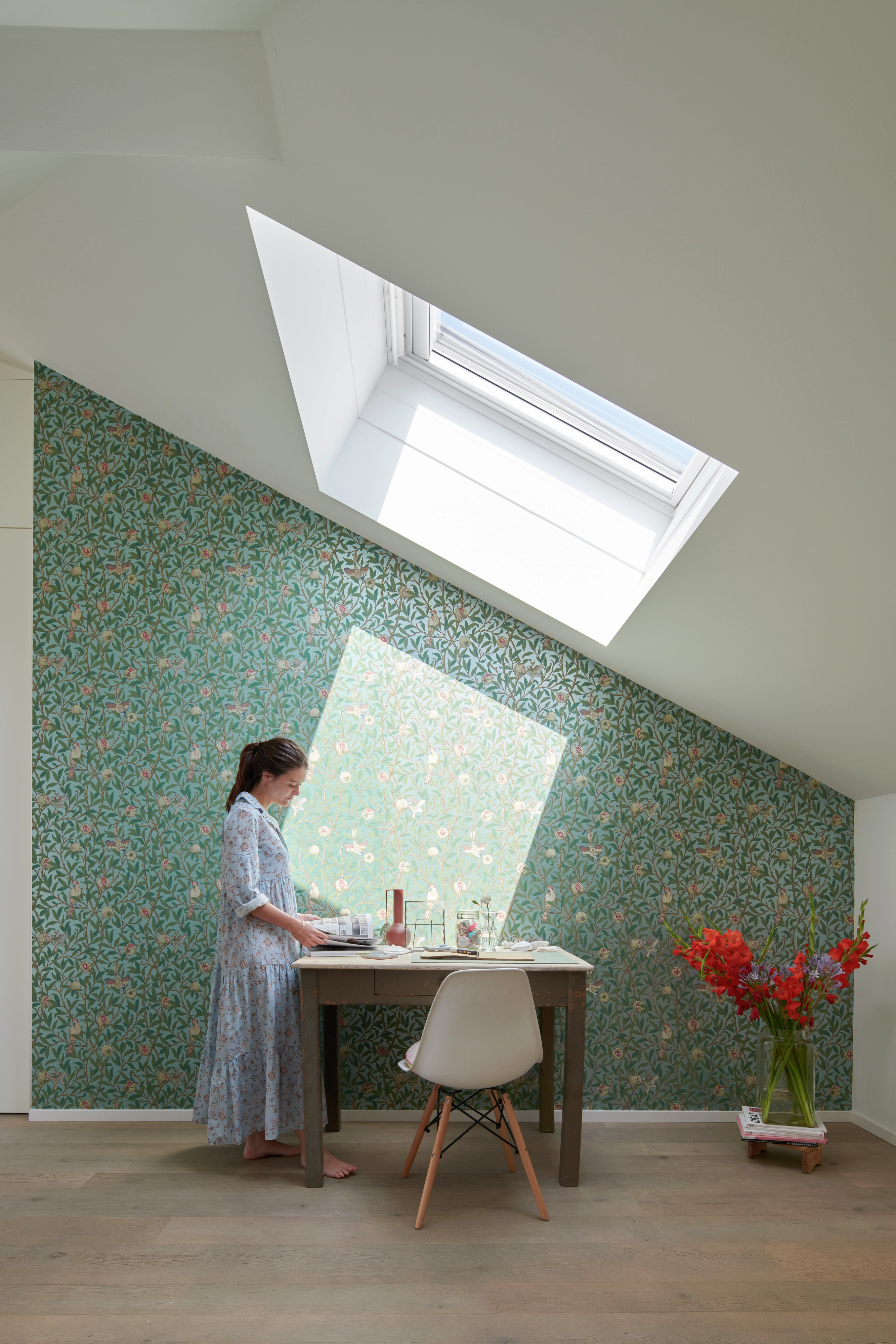 Bureau à domicile avec fenêtre de toit VELUX, papier peint floral et sol en bois.