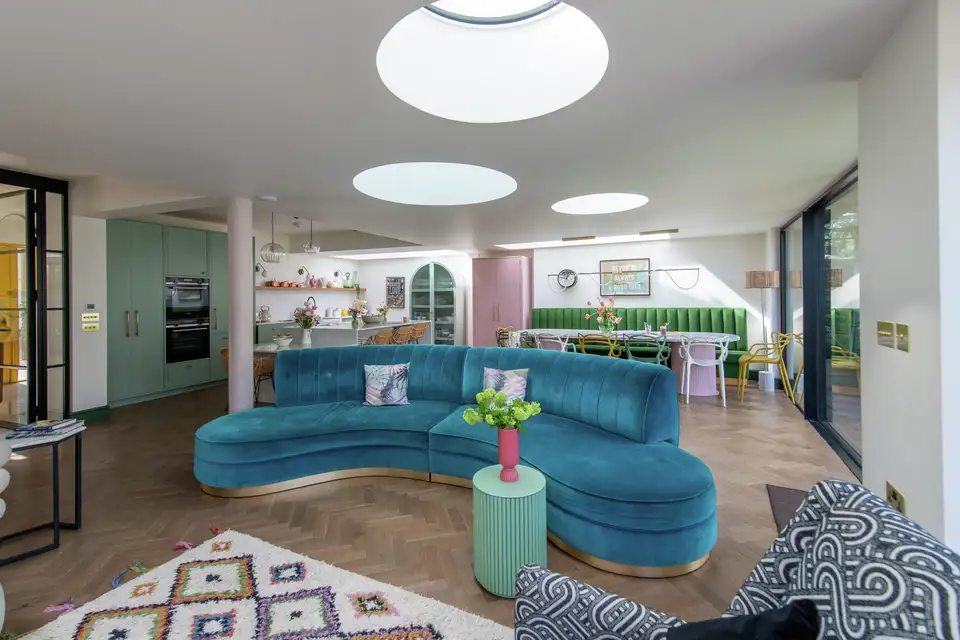 Canapé incurvé en velours turquoise avec coussins colorés dans un salon au style années 80. 