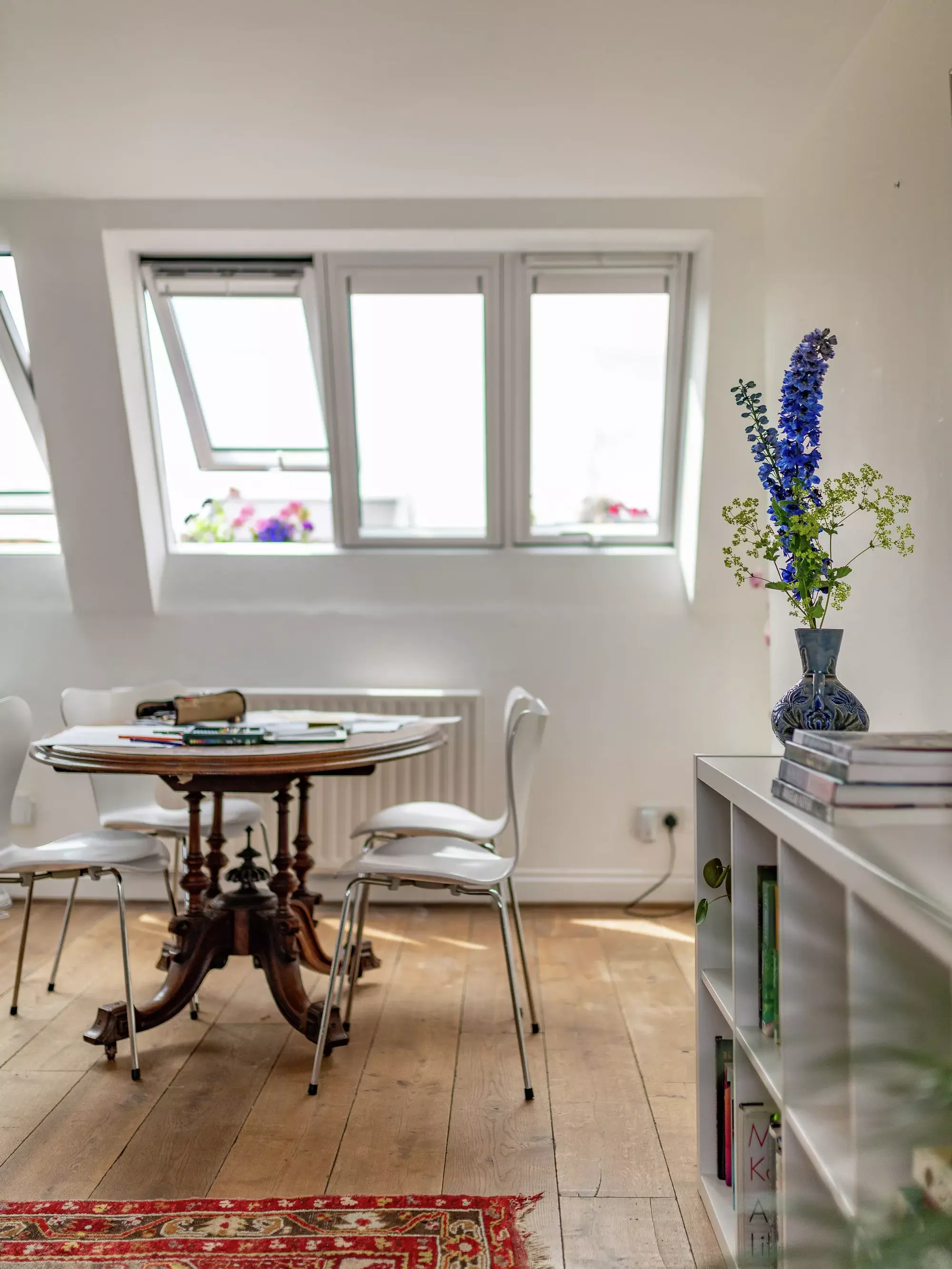 Bureau à domicile dans le comble avec des fenêtres VELUX, une table en bois, des chaises blanches et un tapis rouge.
