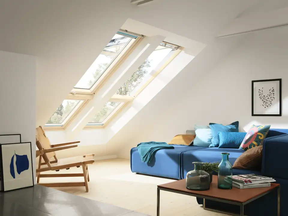 Salon sous combles avec fenêtres de toit, canapé bleu et mobilier épuré.