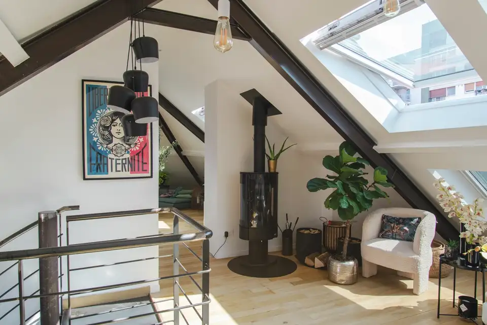Un espace loft élégant avec quatre fenêtres de toit VELUX, une cheminée moderne, un fauteuil confortable et une décoration vibrante sous une lumière naturelle abondante.