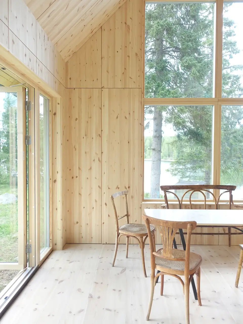 Interiør af sommerhus med lyst trævægge og store vinduer med udsigt til søen