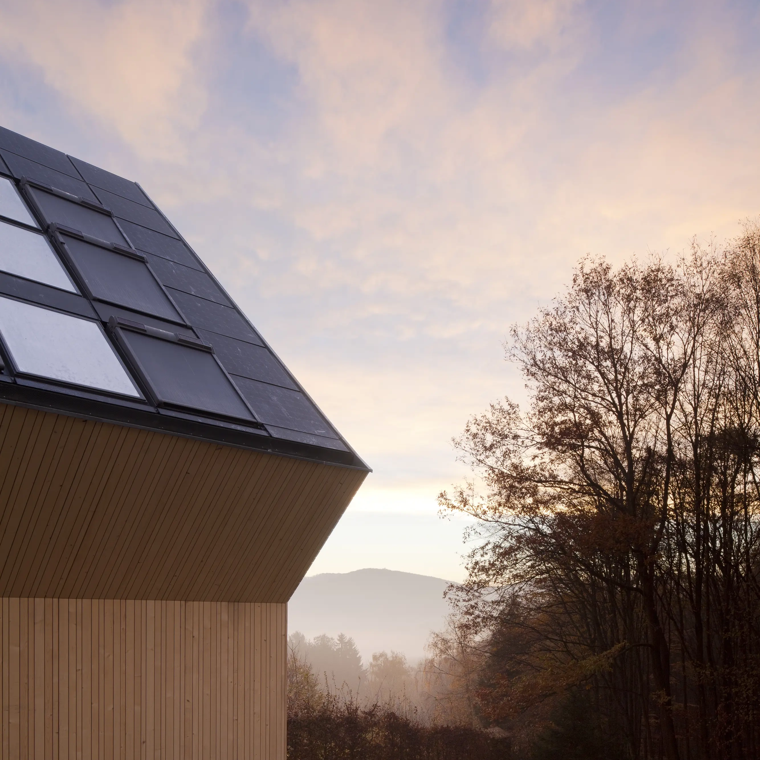 Modern building with solar panels on the roof, surrounded by trees.