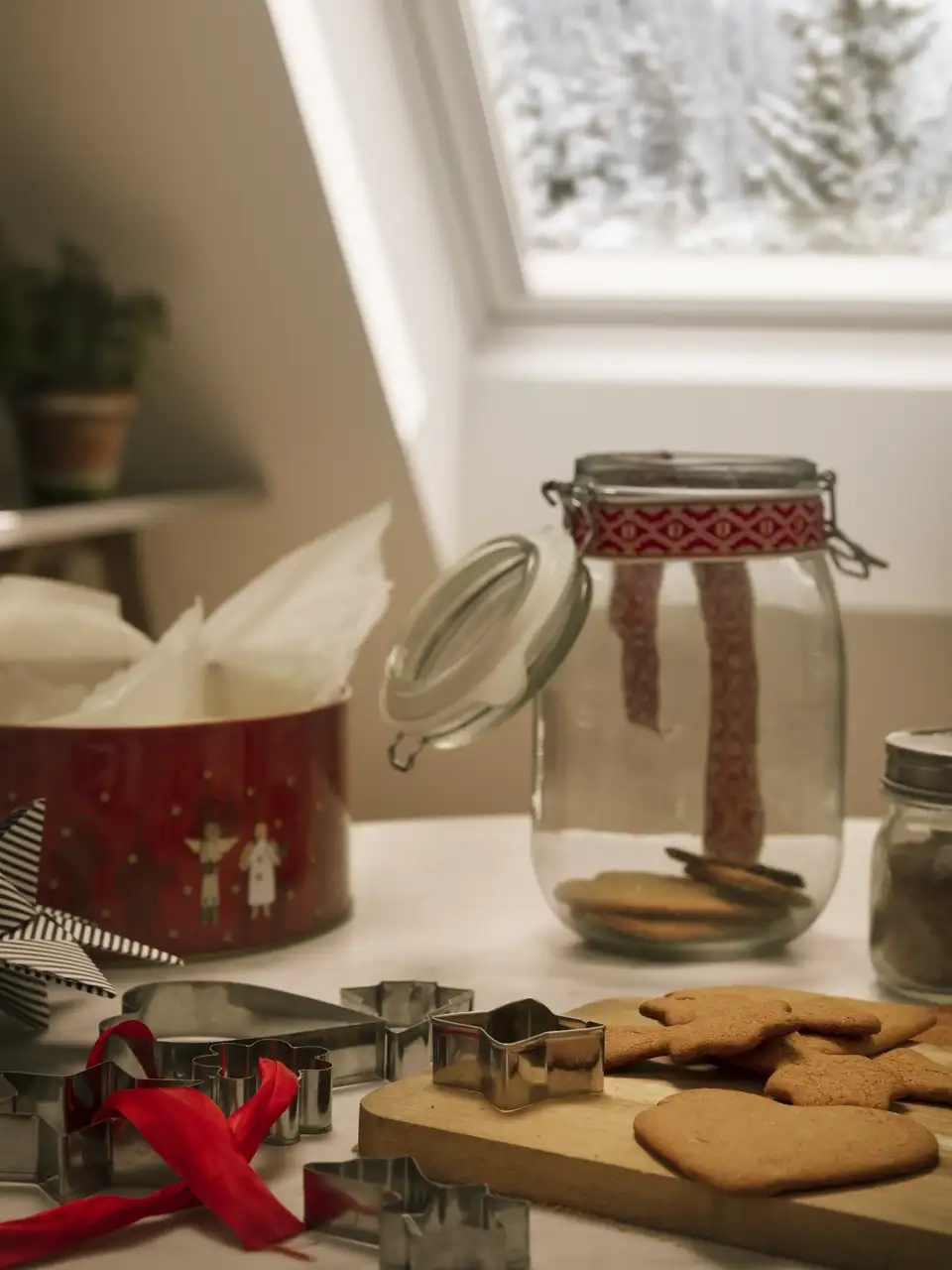 Biscotti natalizi su un tagliere, stampi e nastri rossi illuminati dalla luce naturale di una finestra per tetti VELUX.