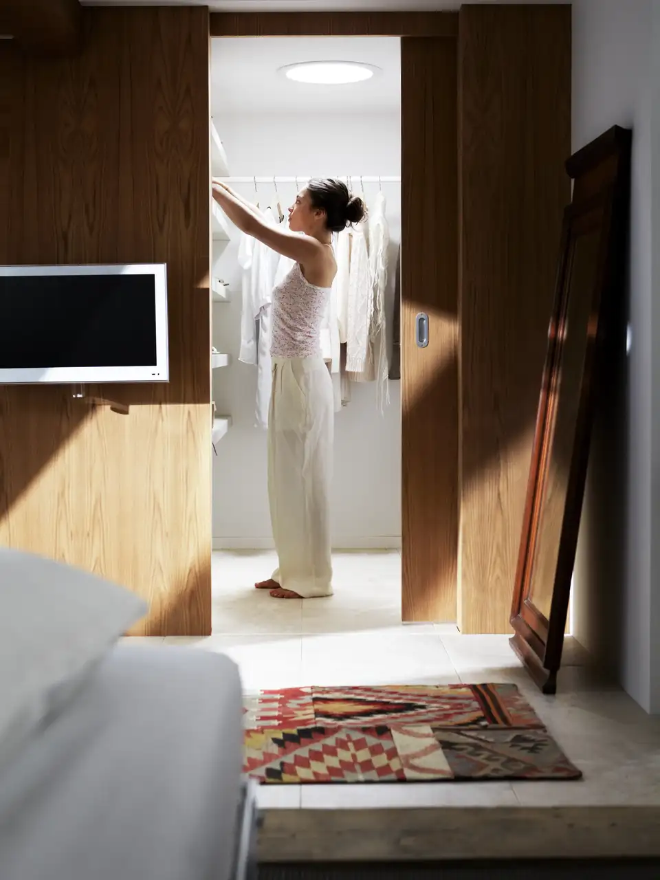 Femme prenant des vêtements dans un dressing mansardé avec lumière naturelle par tunnel solaire. 