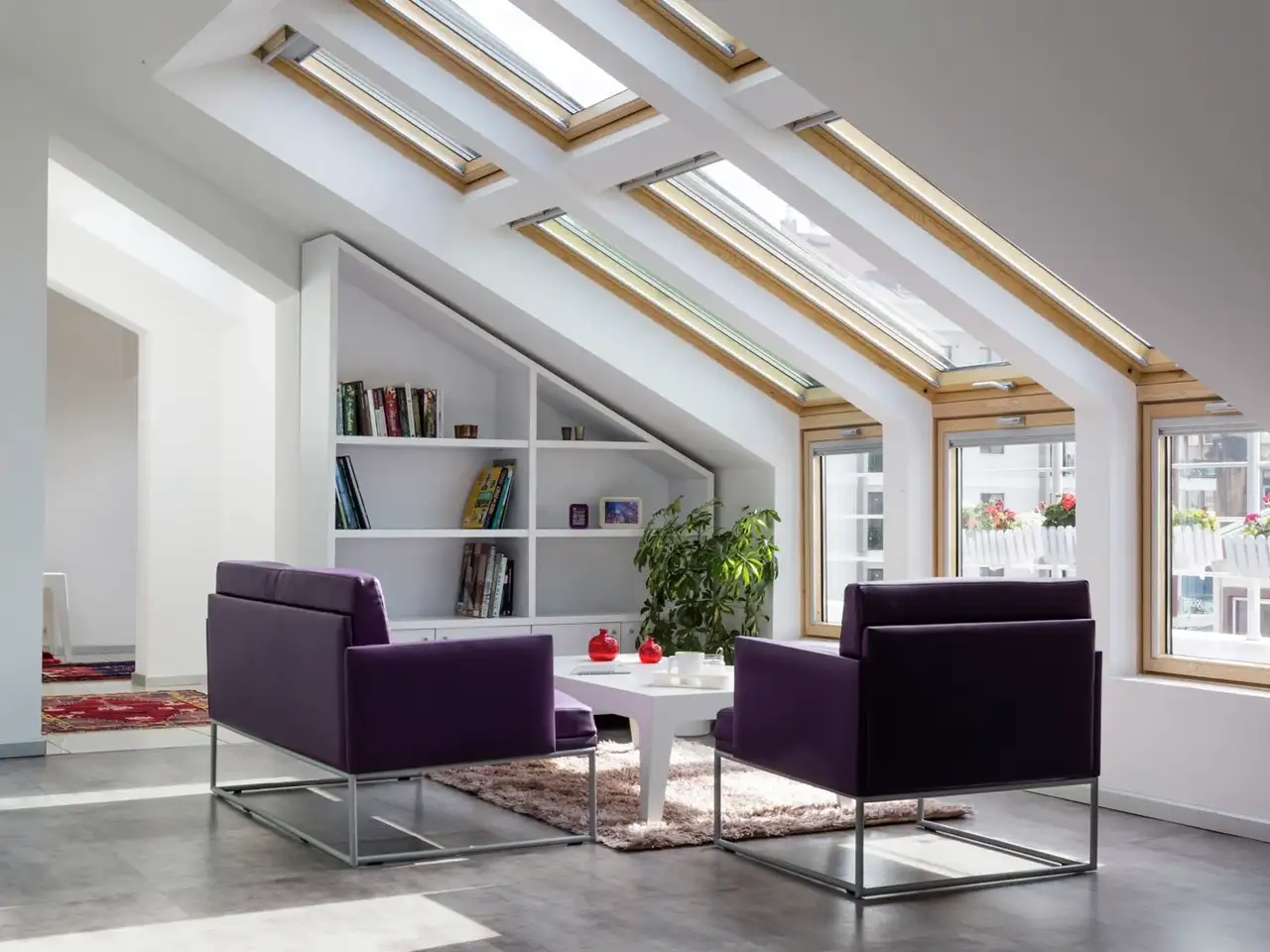 Soggiorno in mansarda con finestre per tetti VELUX, poltrone viola e libreria.