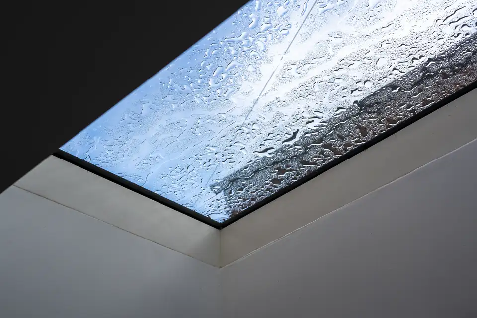 Ventana de cubierta plana VELUX con gotas de lluvia en el exterior del cristal.    
