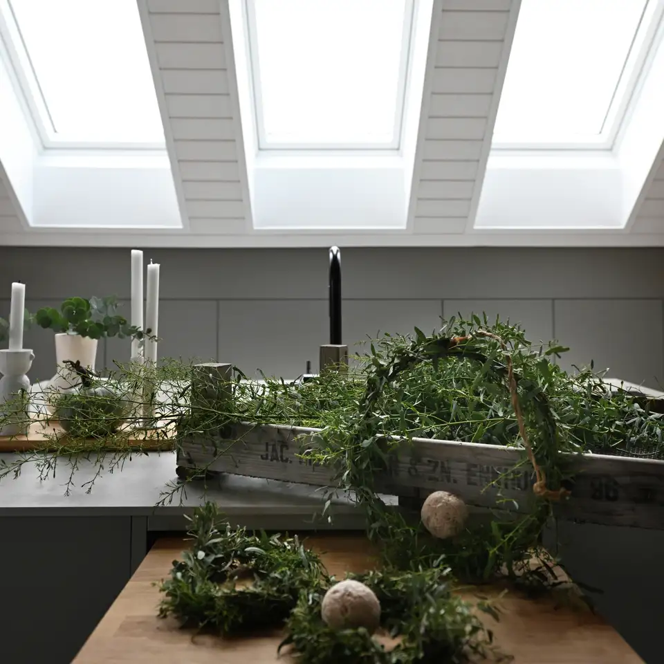 Composizioni con rami verdi e ghirlande artigianali illuminate dalla luce naturale delle finestre per tetti VELUX.